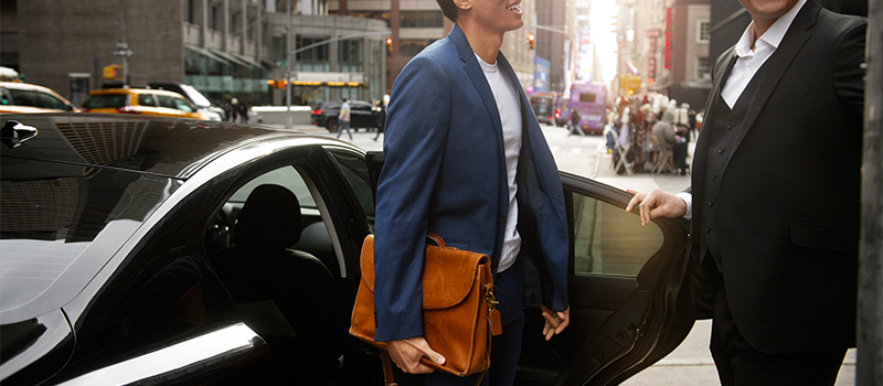 Chauffeur assisting a passenger beside an executive car for an airport transfer